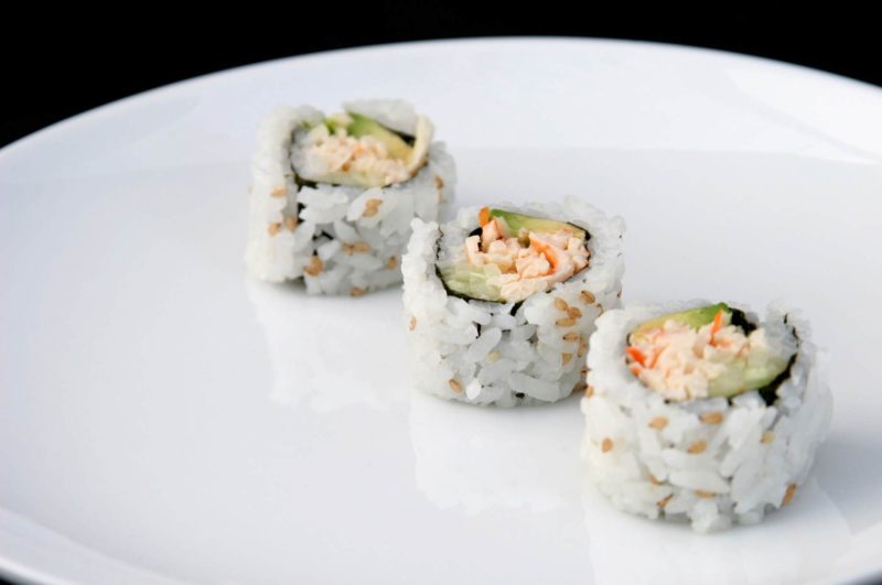 California roll diagonal on white plate with black background.